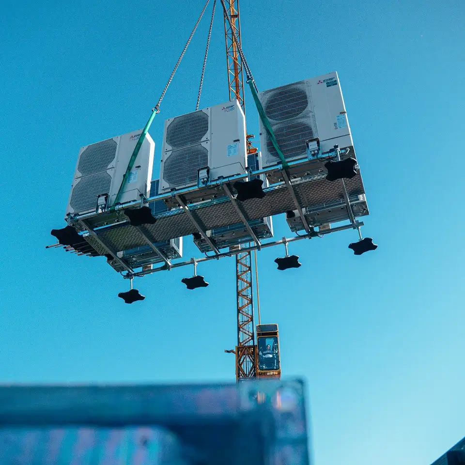Prefab frame met drie buitenunits hangt aan de kraan tijdens het hijsen naar het dak