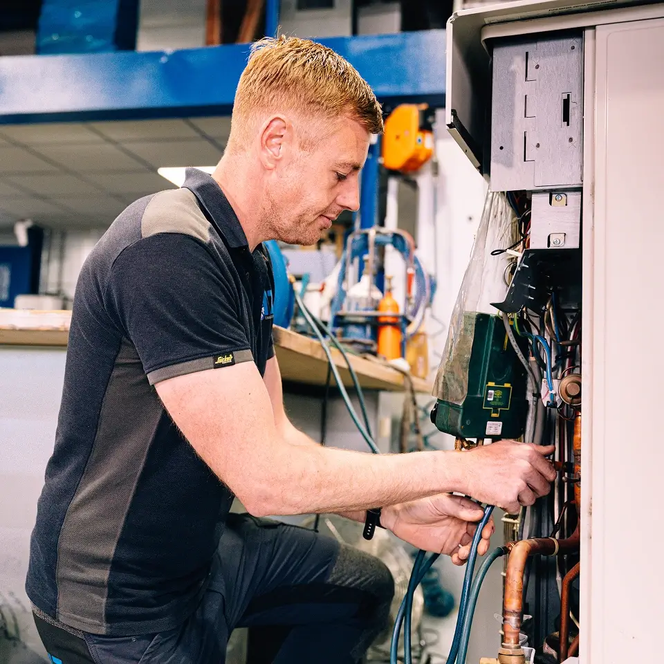 Monteur werkt aan de koperen leidingen en bedrading in een geopende unit in de werkplaats